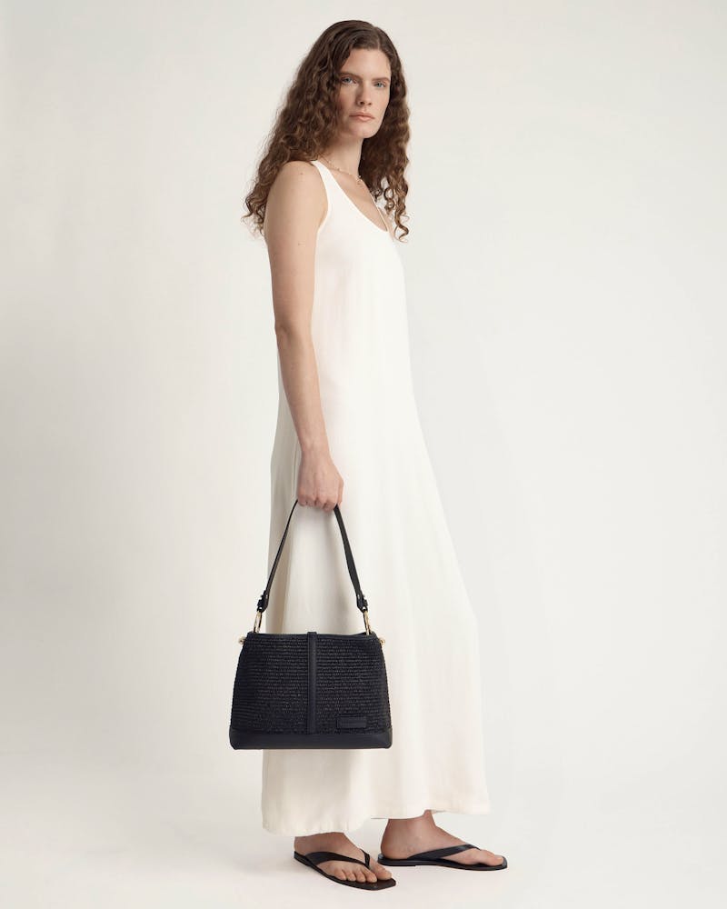 Model in white maxi dress holding a black raffia hobo bag by hand.