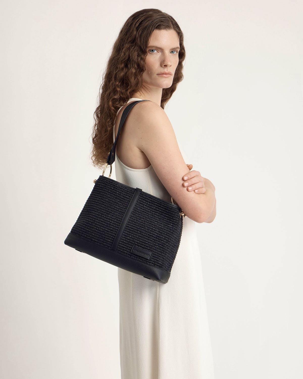 Woman in white dress carrying black raffia hobo bag on shoulder.