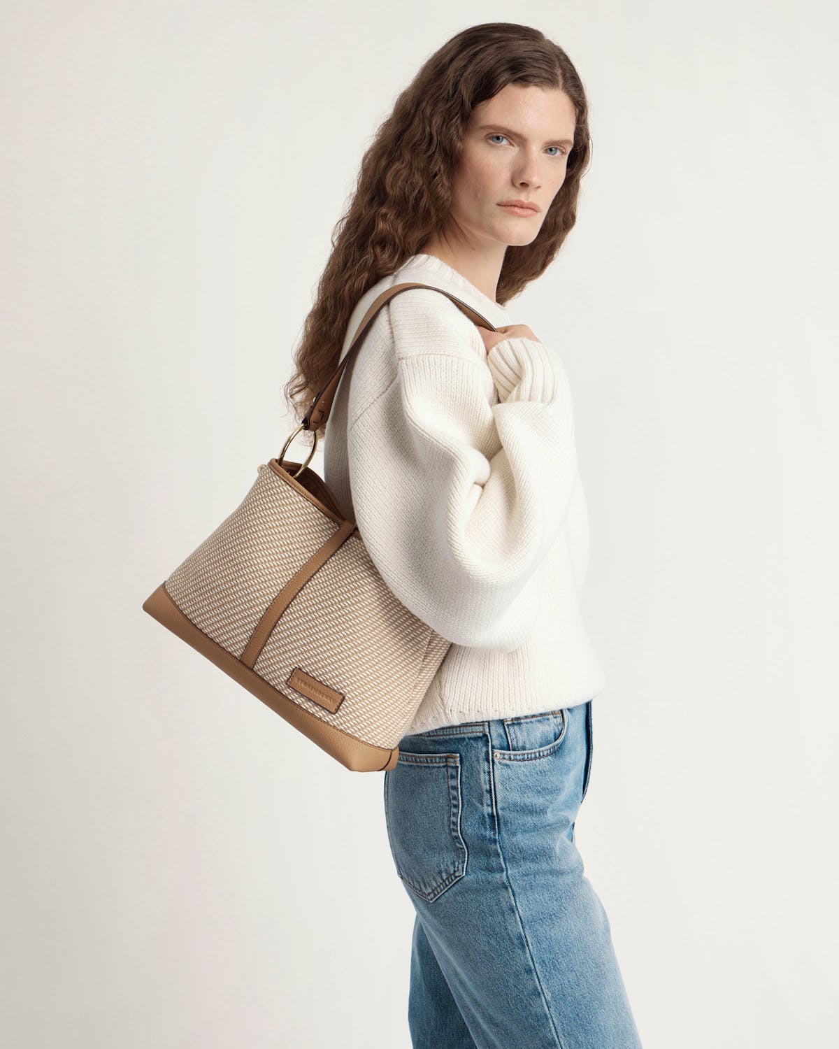 Model wearing white jumper and jeans carries caramel and natural twill hobo bag.