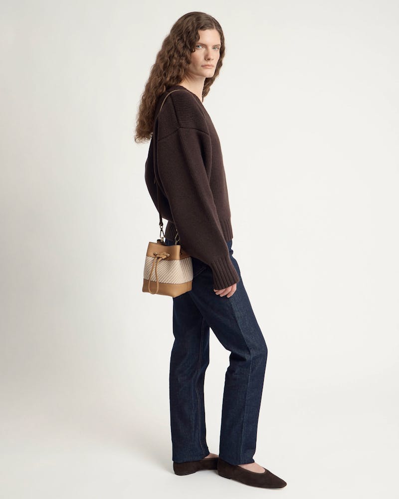Woman in dark jumper and jeans carries caramel and natural twill bucket bag.