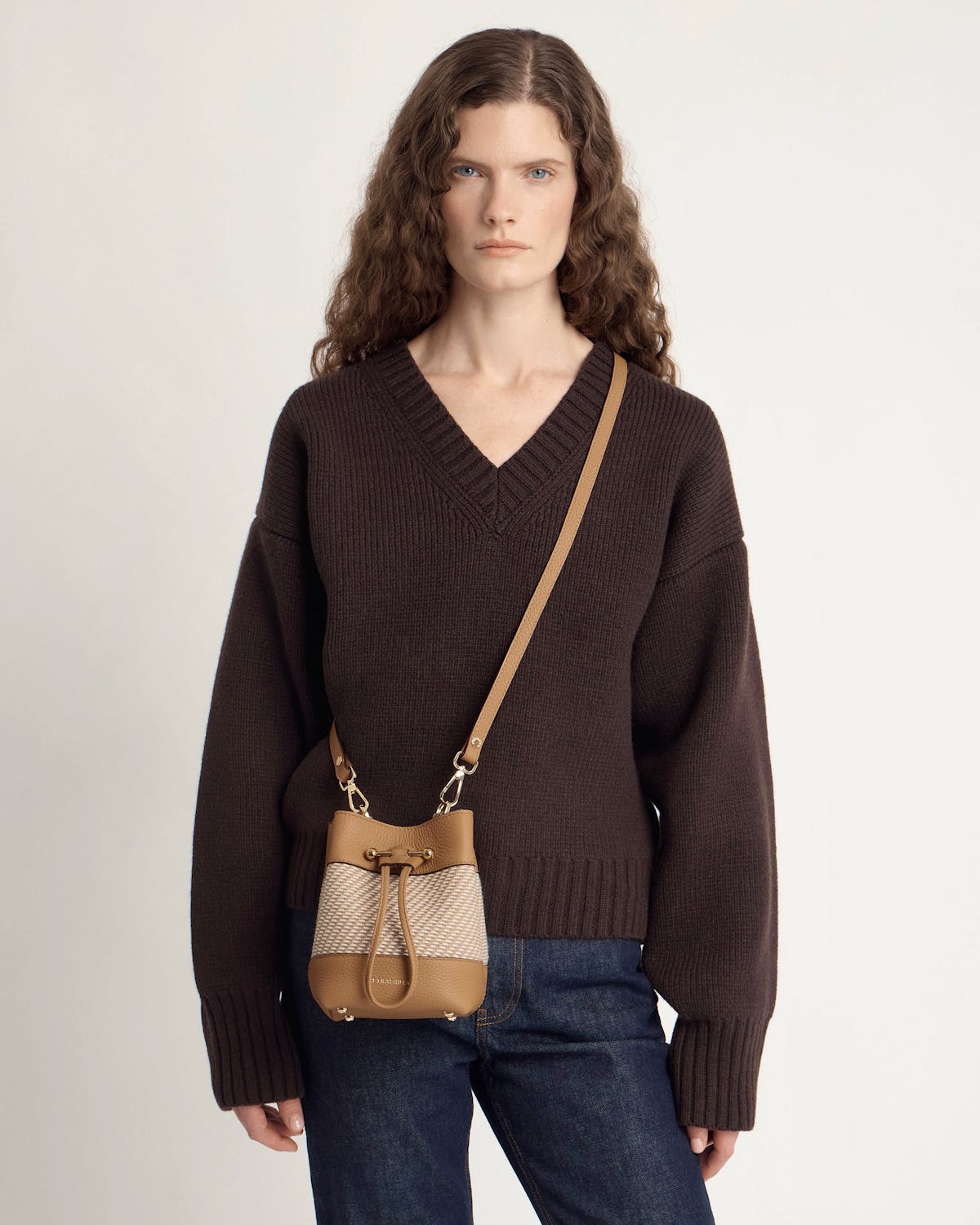 Woman wearing a caramel and natural twill bucket crossbody bag over dark brown jumper.