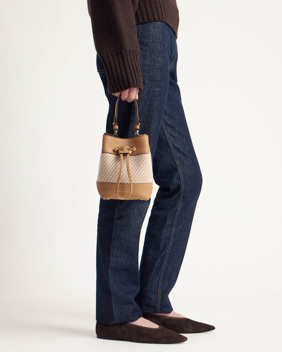 Model holding caramel and natural twill bucket bag at side.