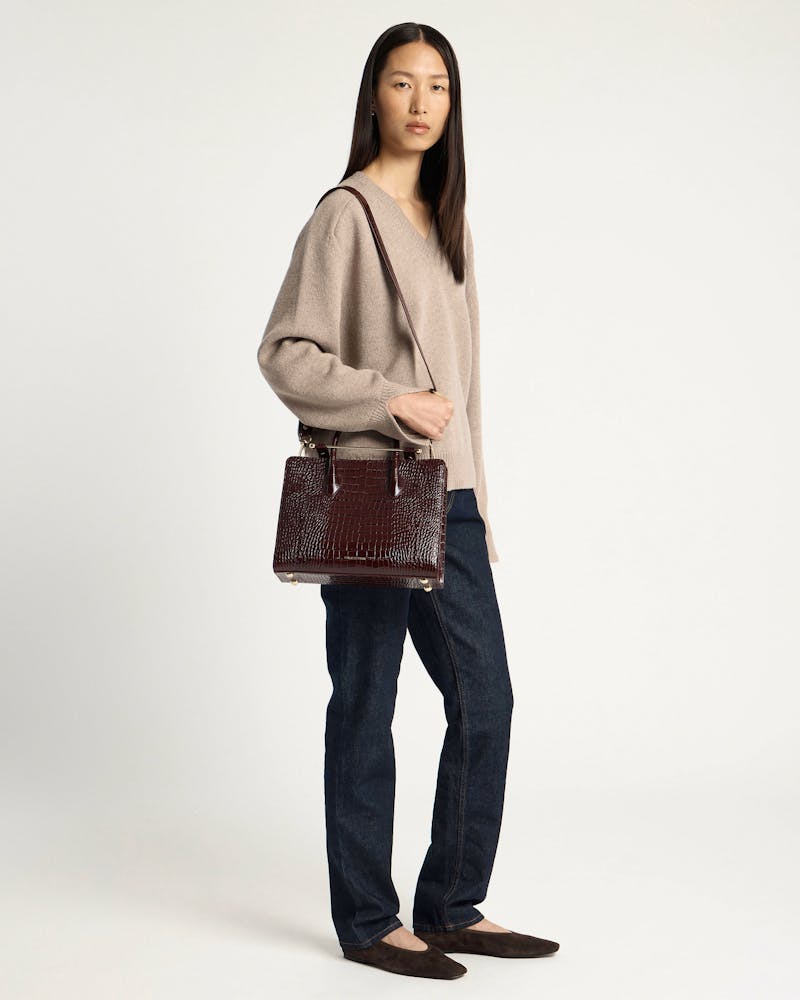 Woman wearing a beige sweater and jeans holding a croc-embossed midi tote bag.