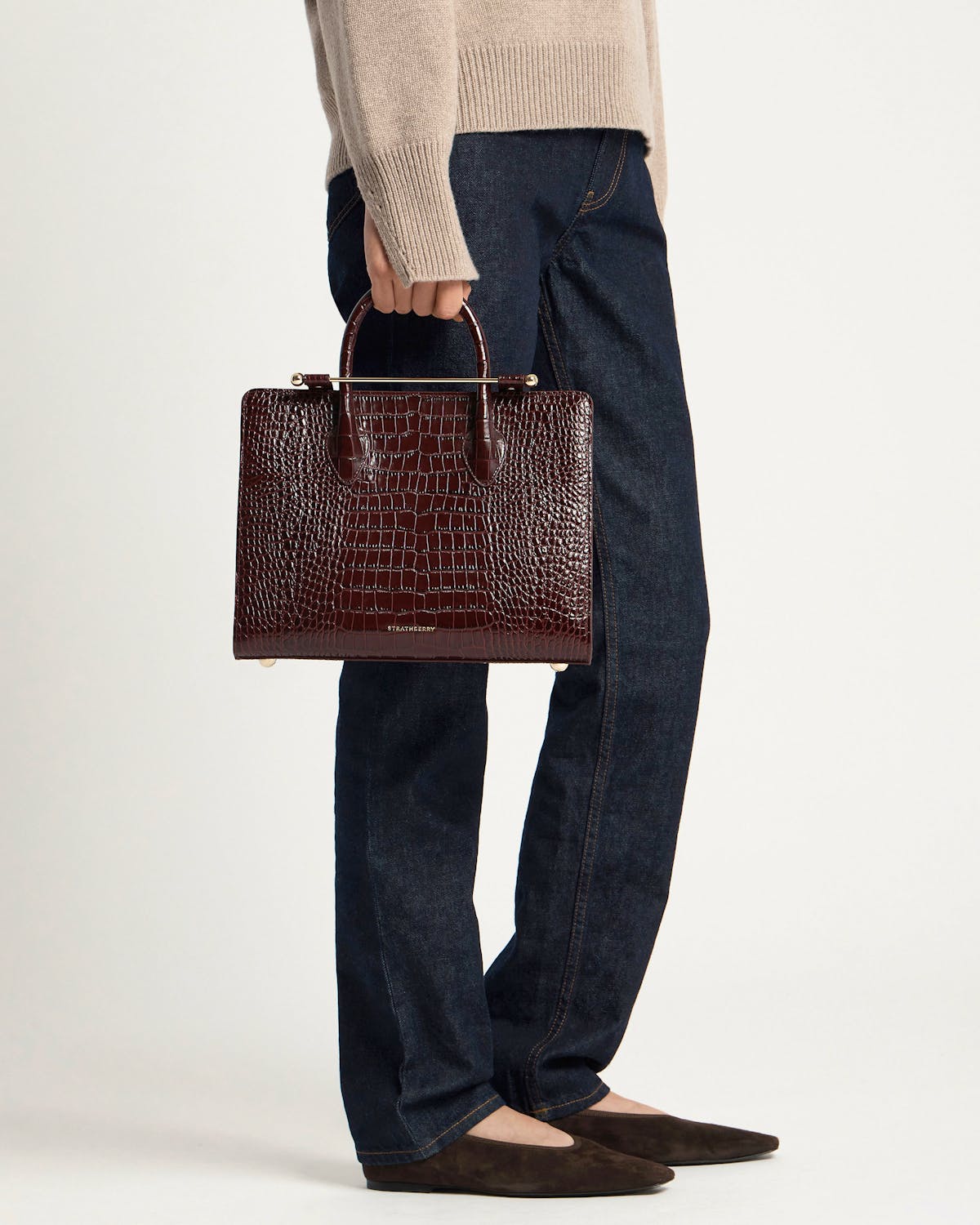 Model holding Strathberry croc-embossed midi tote in dark brown with gold hardware
