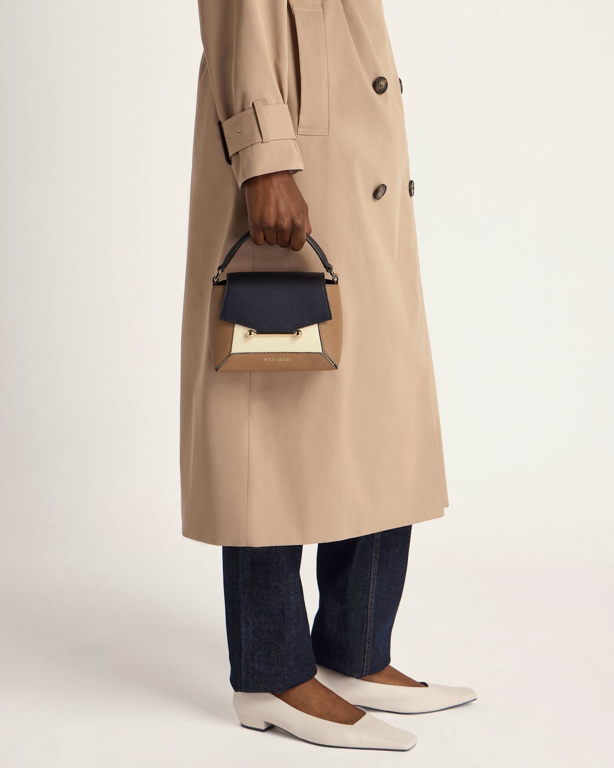 Model holding Strathberry Mosaic Nano top-handle bag in clay, black and white.
