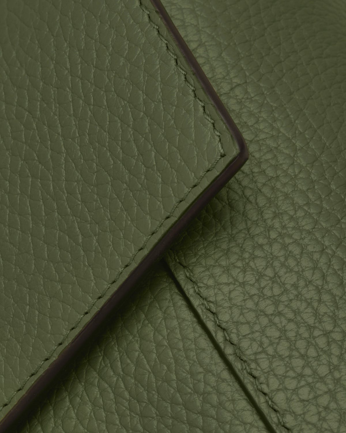 Pine green pebbled leather bag flap with visible stitching and edge detail.