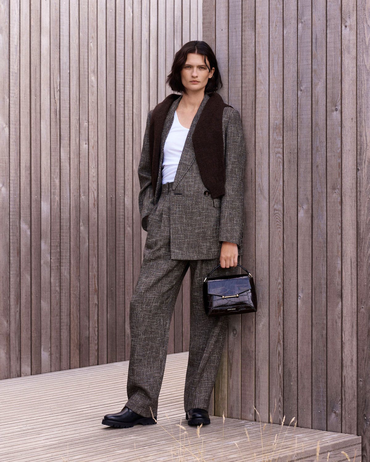 Woman in tailored checked suit holding small croc-effect mosaic handbag by handle.