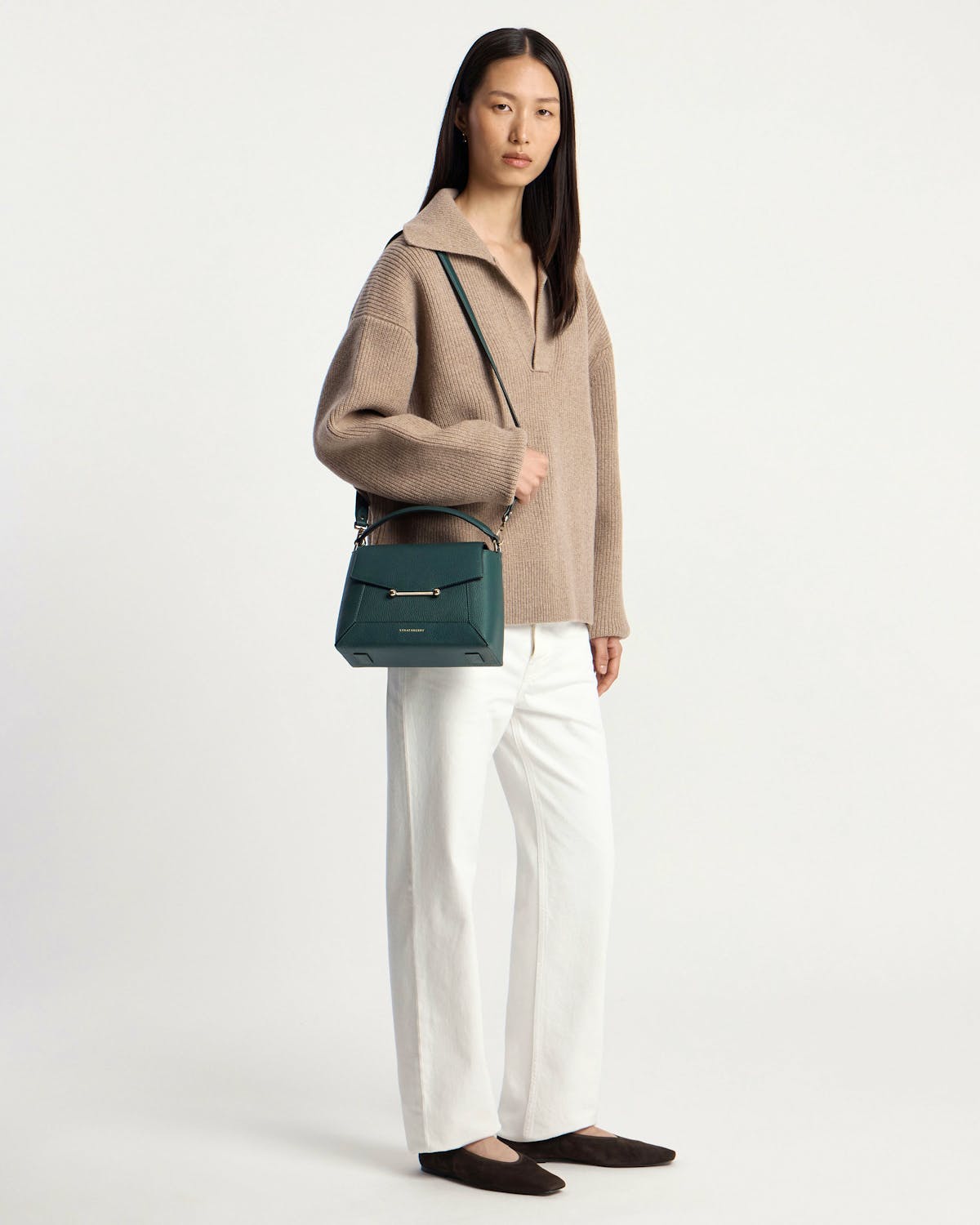 Model wearing beige jumper and white trousers holding bottle green mosaic bag.