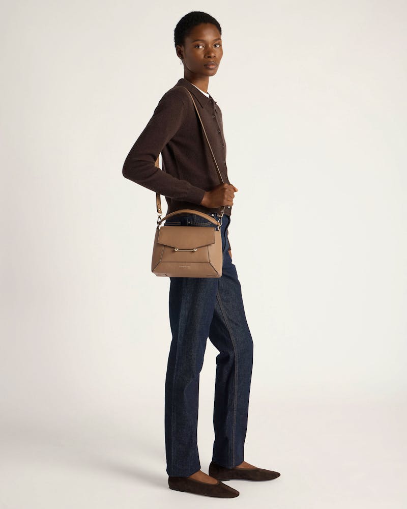 Model wearing clay mosaic crossbody bag with top handle and flap, dark jeans, brown flats