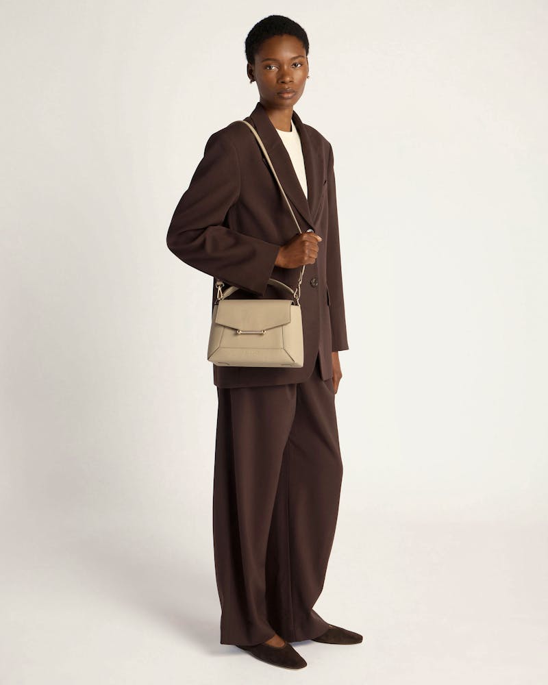 Model in brown suit carrying a sand-coloured mosaic bag by its top handle.