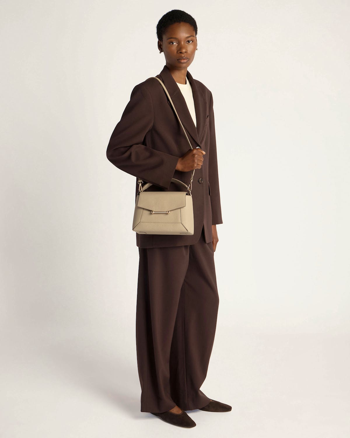 Model in brown suit carrying a sand-coloured mosaic bag by its top handle.