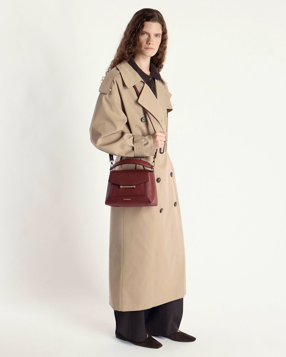 Model in beige trench coat holding an oxblood mosaic bag by the handle.