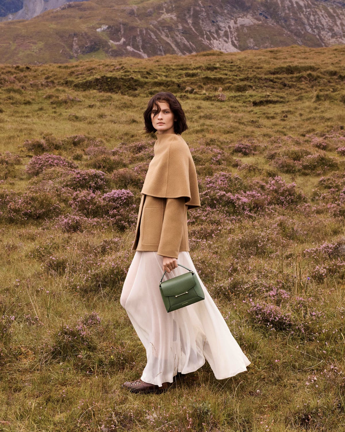 Model walking in a field holding a pine green mosaic top-handle bag.