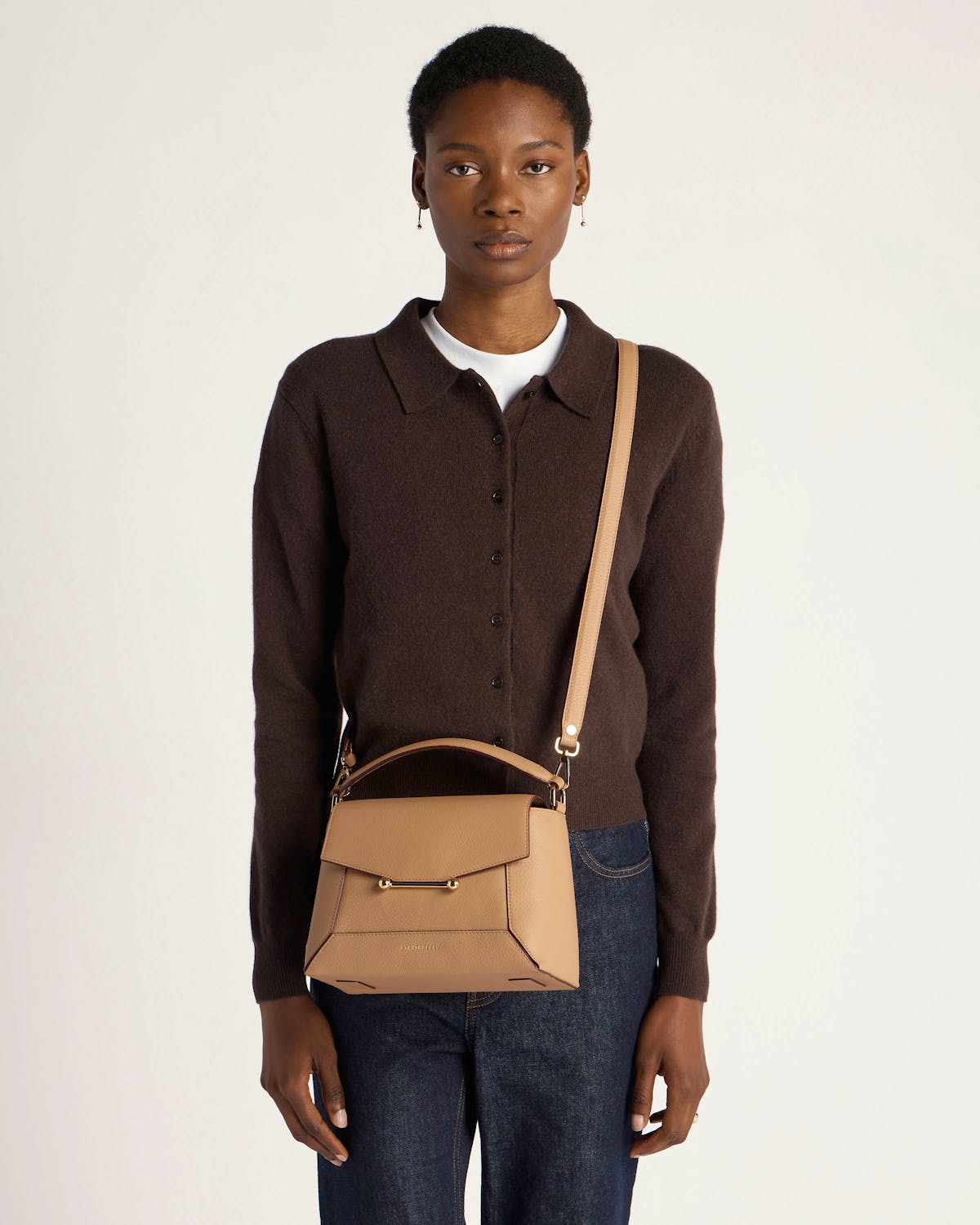 Woman wearing dark brown cardigan and jeans carrying a caramel mosaic crossbody bag.