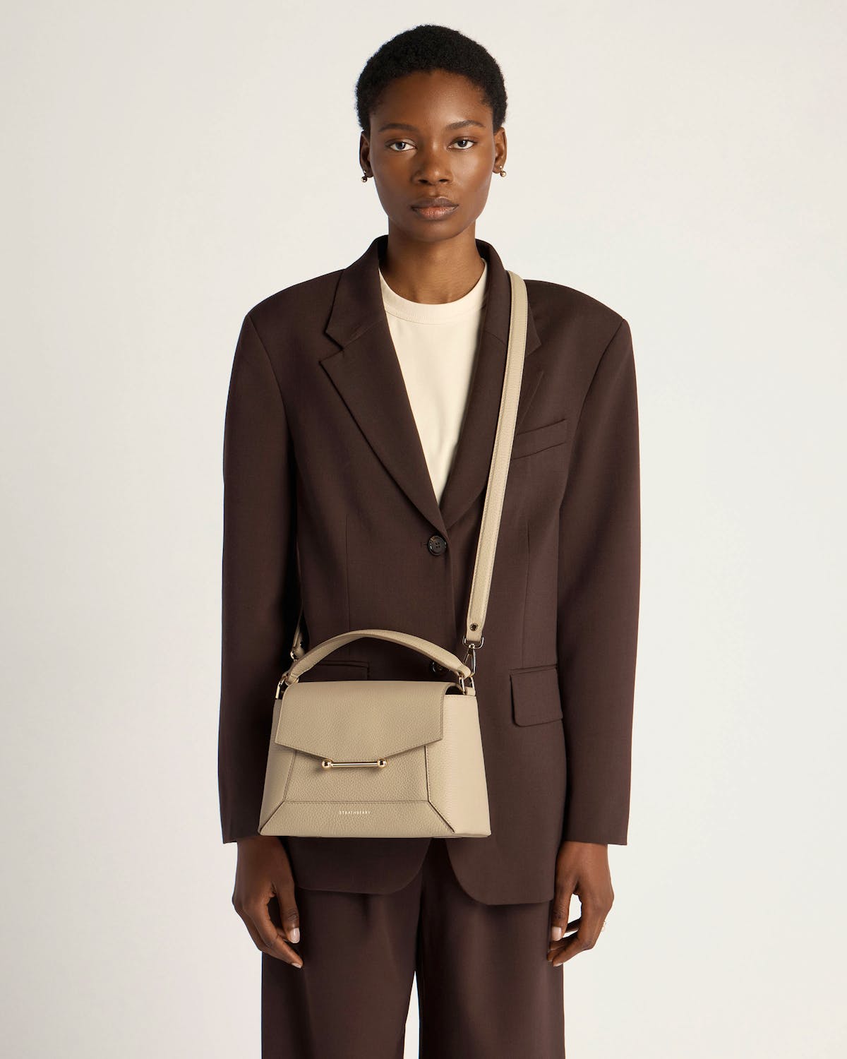 Model wearing a sand mosaic bag with top handle and long shoulder strap.