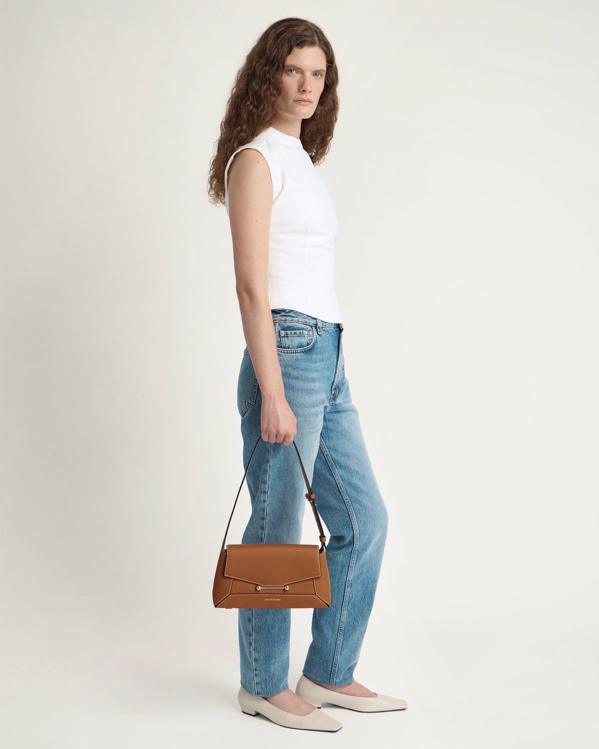 Model holding tan mosaic shoulder bag by hand, wearing white sleeveless top and blue jeans.