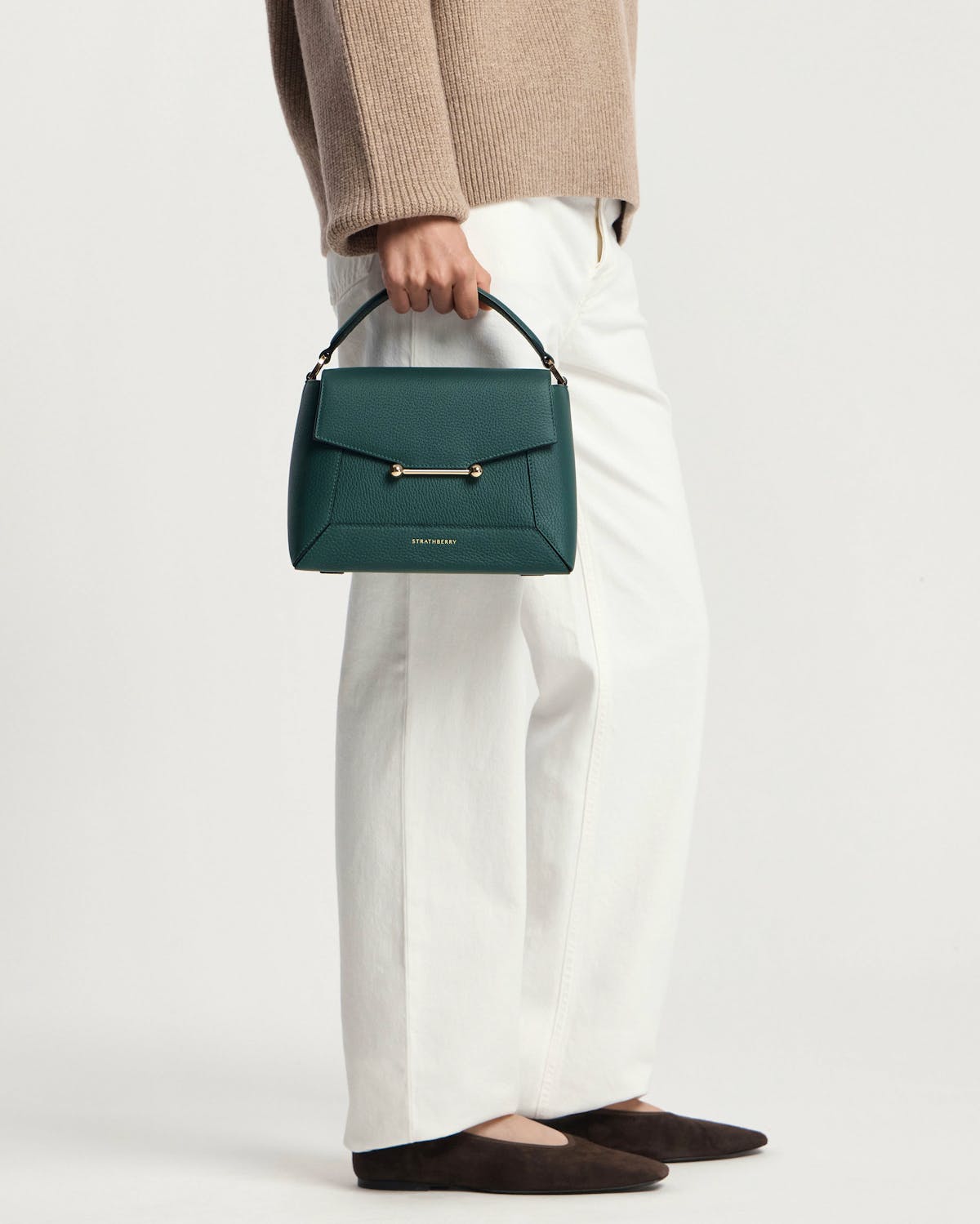 Model carrying bottle green Strathberry mosaic bag by the top handle.
