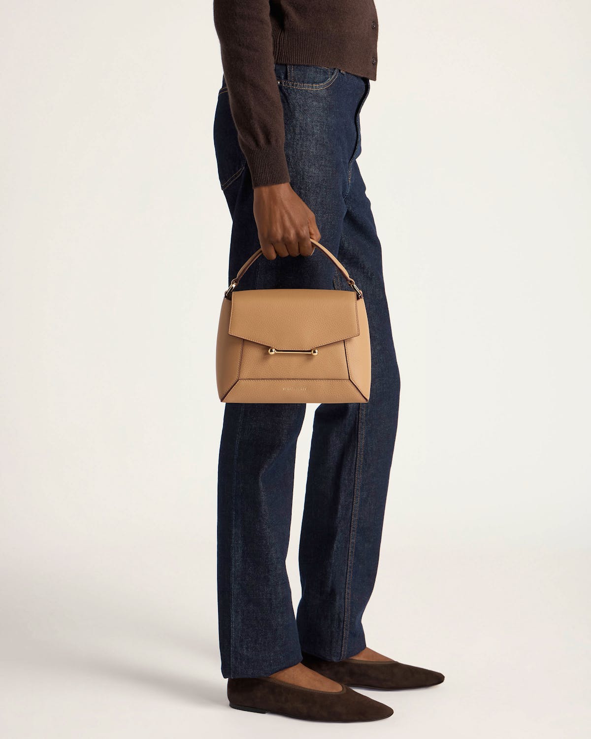 Model holding caramel mosaic bag by the top handle, wearing jeans and brown flats.