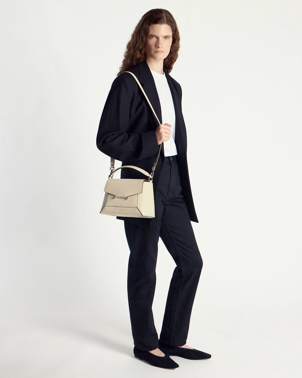 Model in black outfit holding vanilla mosaic bag with top handle and shoulder strap.