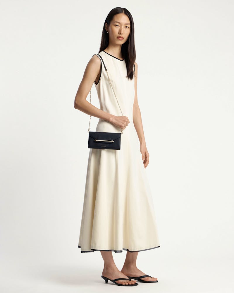 Model in cream sleeveless dress wearing a black chain wallet on a gold shoulder chain.