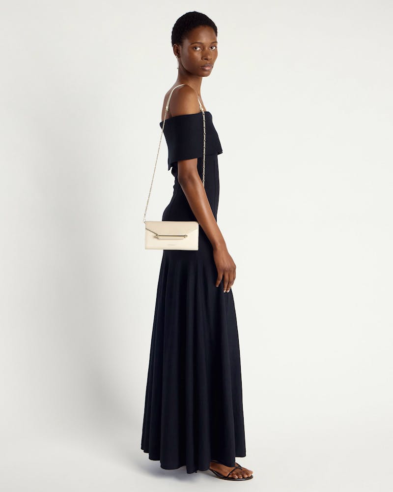 Model wearing black off-shoulder dress carries vanilla diamond chain wallet on shoulder.