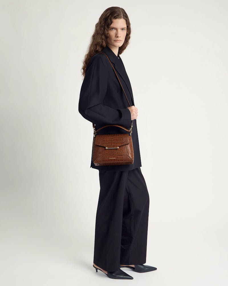 Model in black suit carrying a brown soft-croc mosaic bag on a shoulder strap.