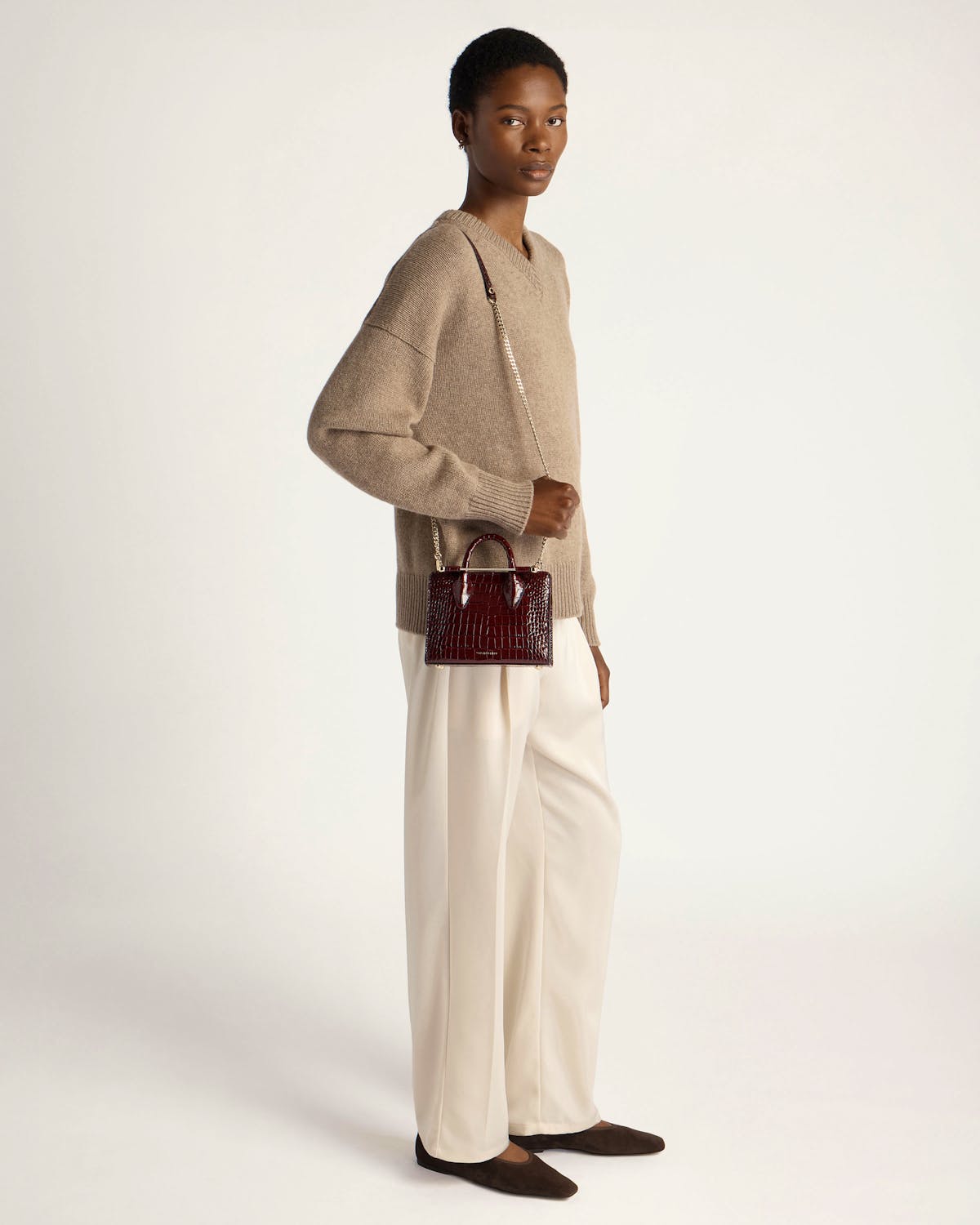 Model wearing beige jumper and cream trousers holding burgundy croc nano tote.