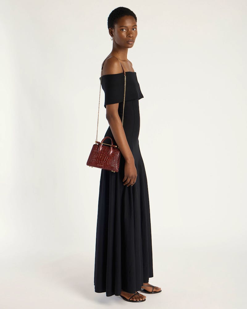 Model in black off-shoulder dress carrying brown croc-embossed nano tote with chain strap.