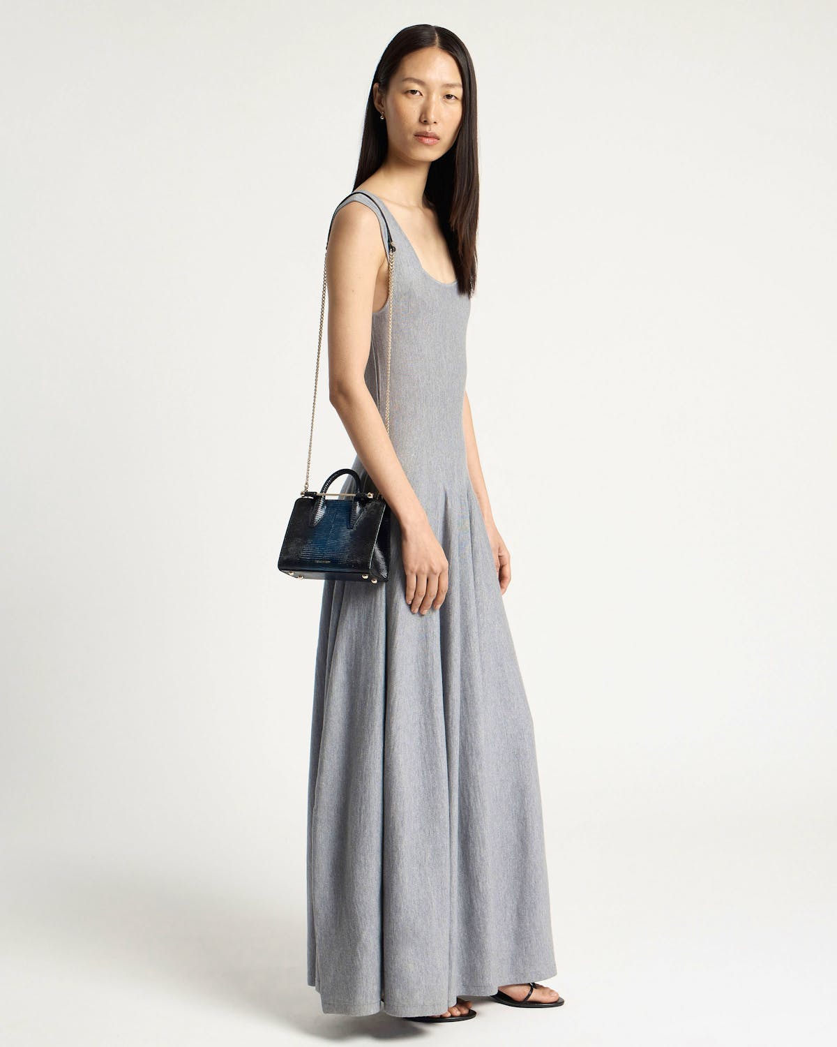 Model in grey maxi dress holding a lizard-effect nano tote with chain strap