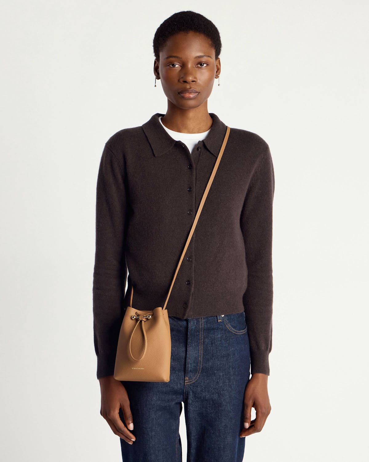 Model wearing a caramel leather drawstring crossbody pouch hanging at hip.