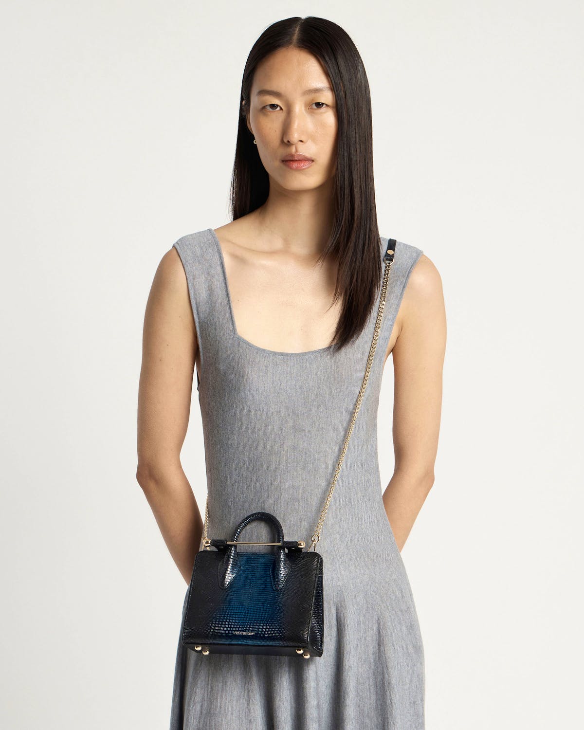 Model wearing small lizard-texture nano tote with top handles and gold chain across body.