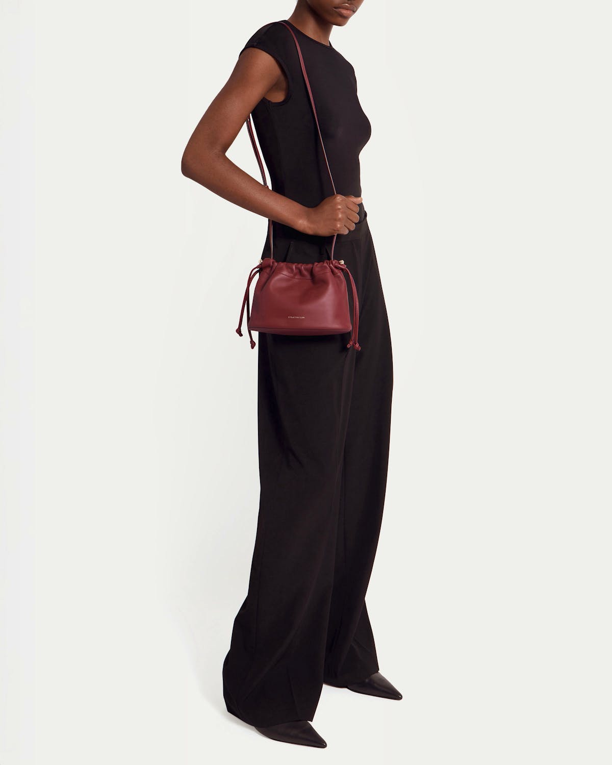 Model wearing black outfit carrying oxblood drawstring shoulder bag worn at hip.