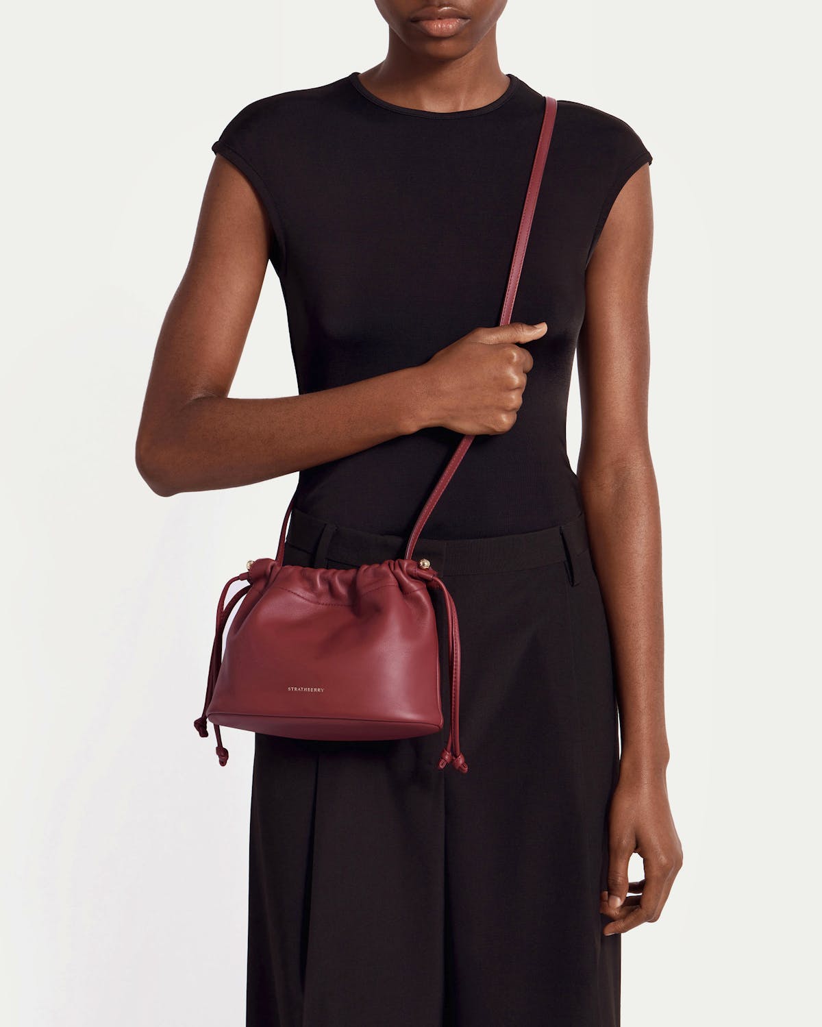 Model in black sleeveless top wearing oxblood Charlotte drawstring bag by Strathberry