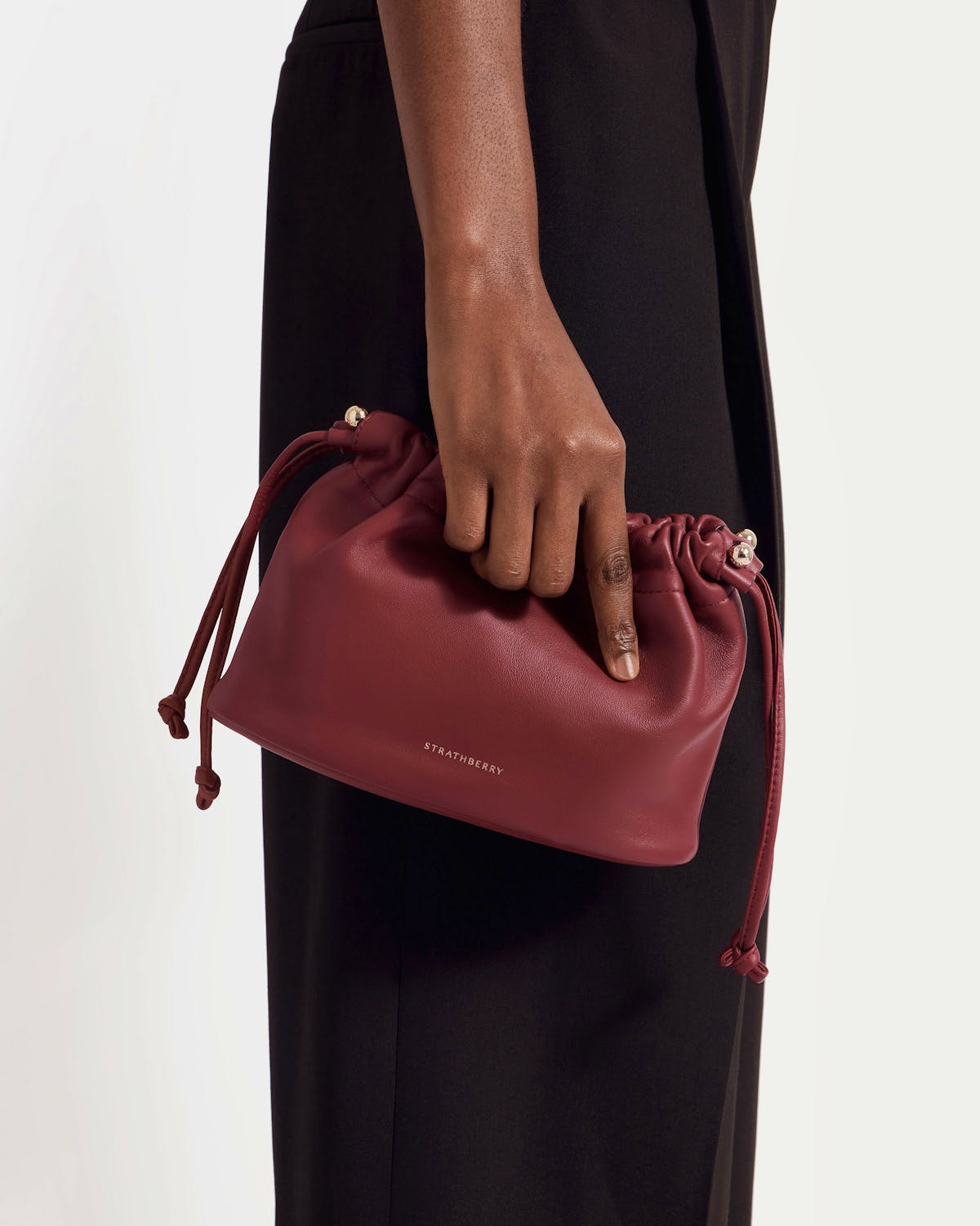 Oxblood leather Charlotte drawstring bag with Strathberry logo held by model's hand.