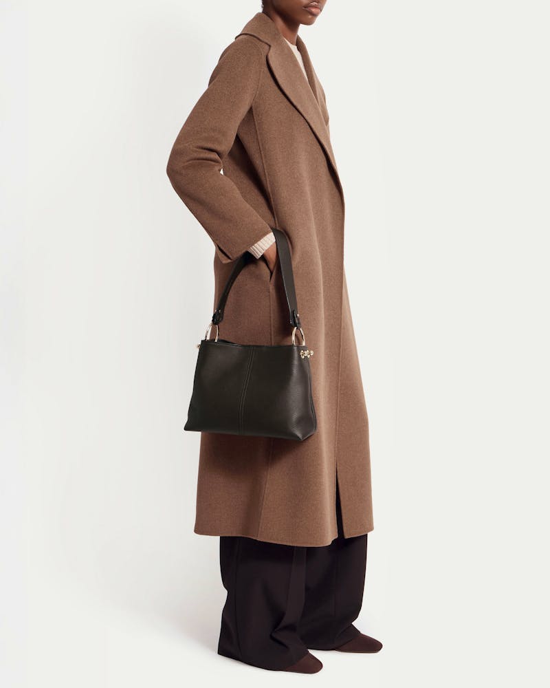 Model wearing a brown coat holding an espresso leather hobo bag by its strap.