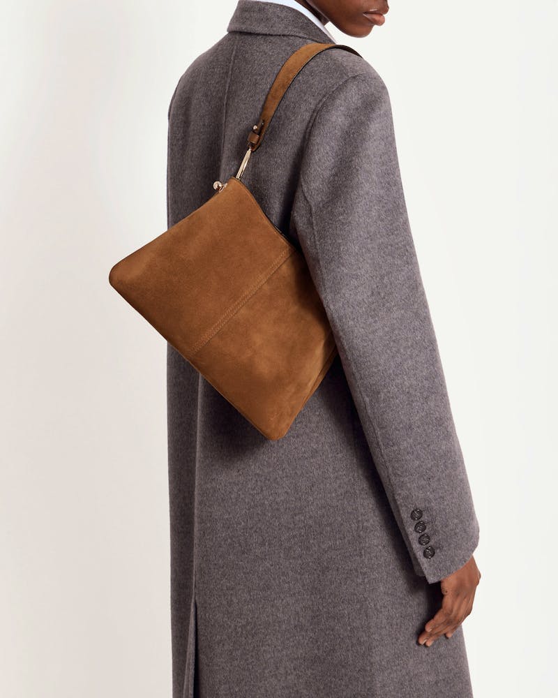 Tan suede hobo bag worn on shoulder by model in grey coat.