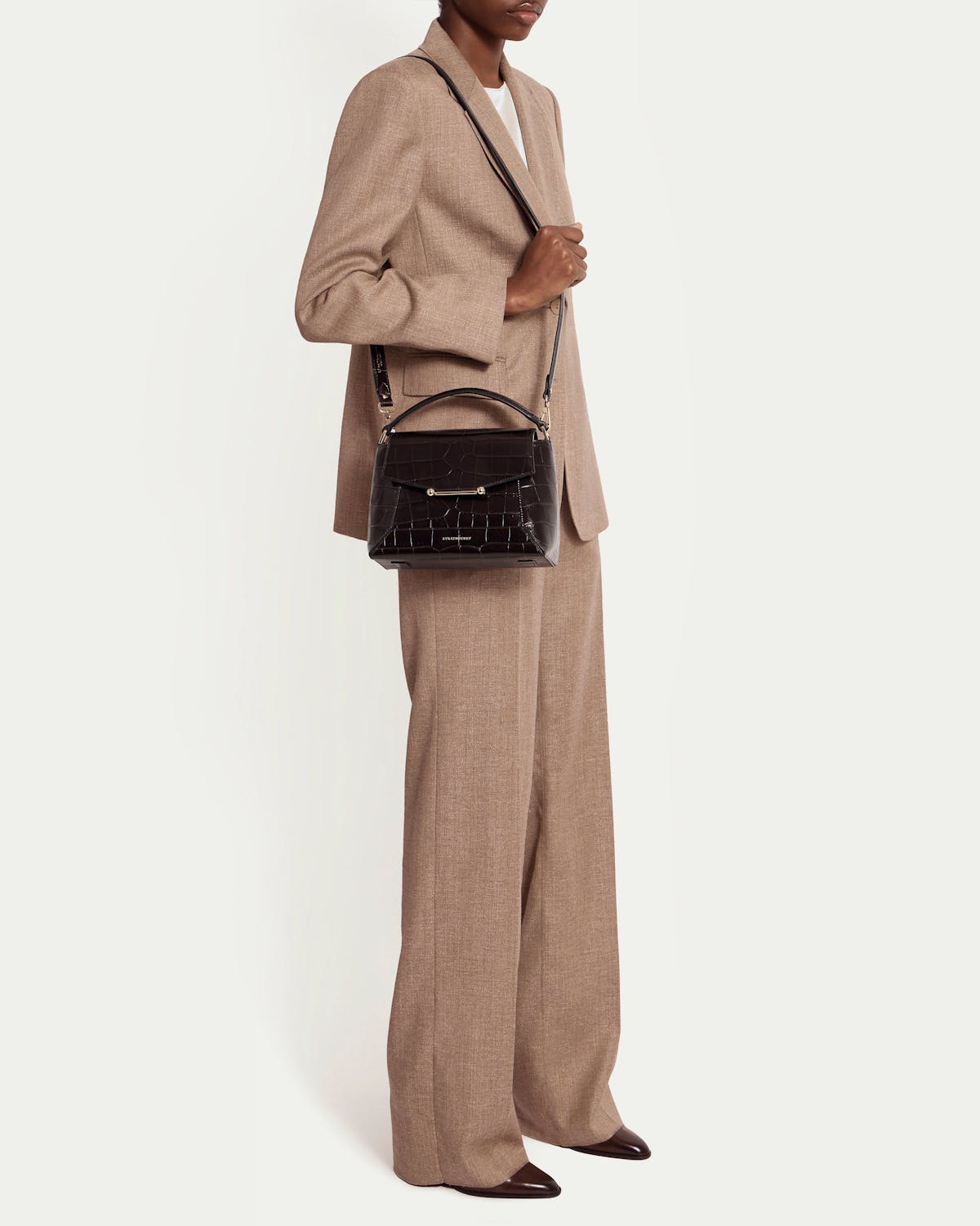 Model in beige suit carries dark croc mosaic bag with top handle and shoulder strap.