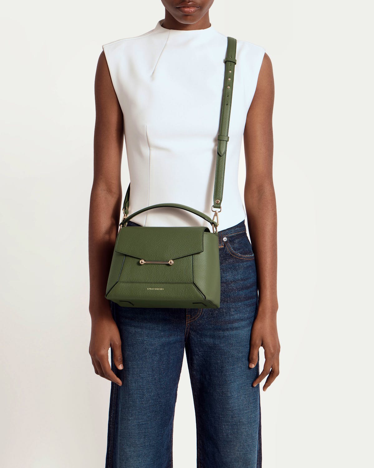 Model wearing a pine green mosaic bag by Strathberry, crossbody with top handle.