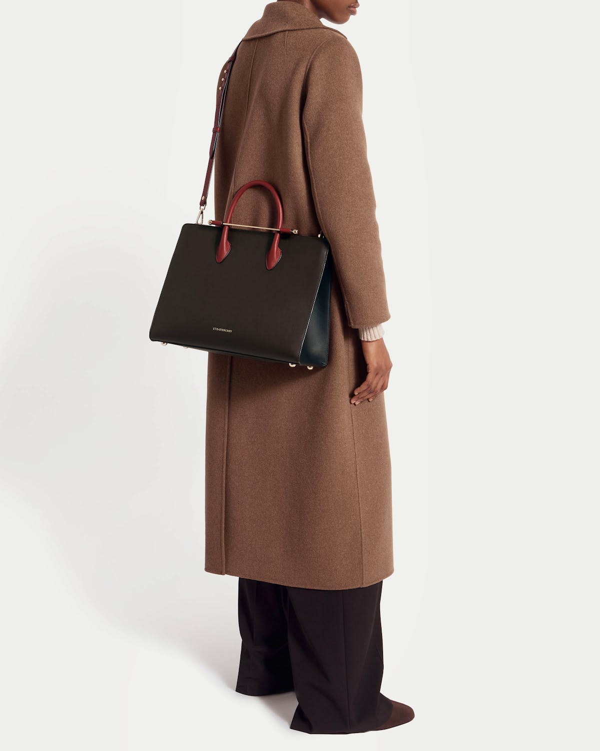 Model wearing a brown coat carrying an espresso, oxblood and black Strathberry tote