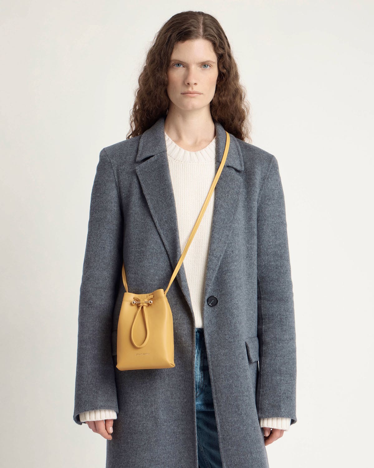 Model wearing a grey coat with a brûlée Osette midi pouch worn crossbody.