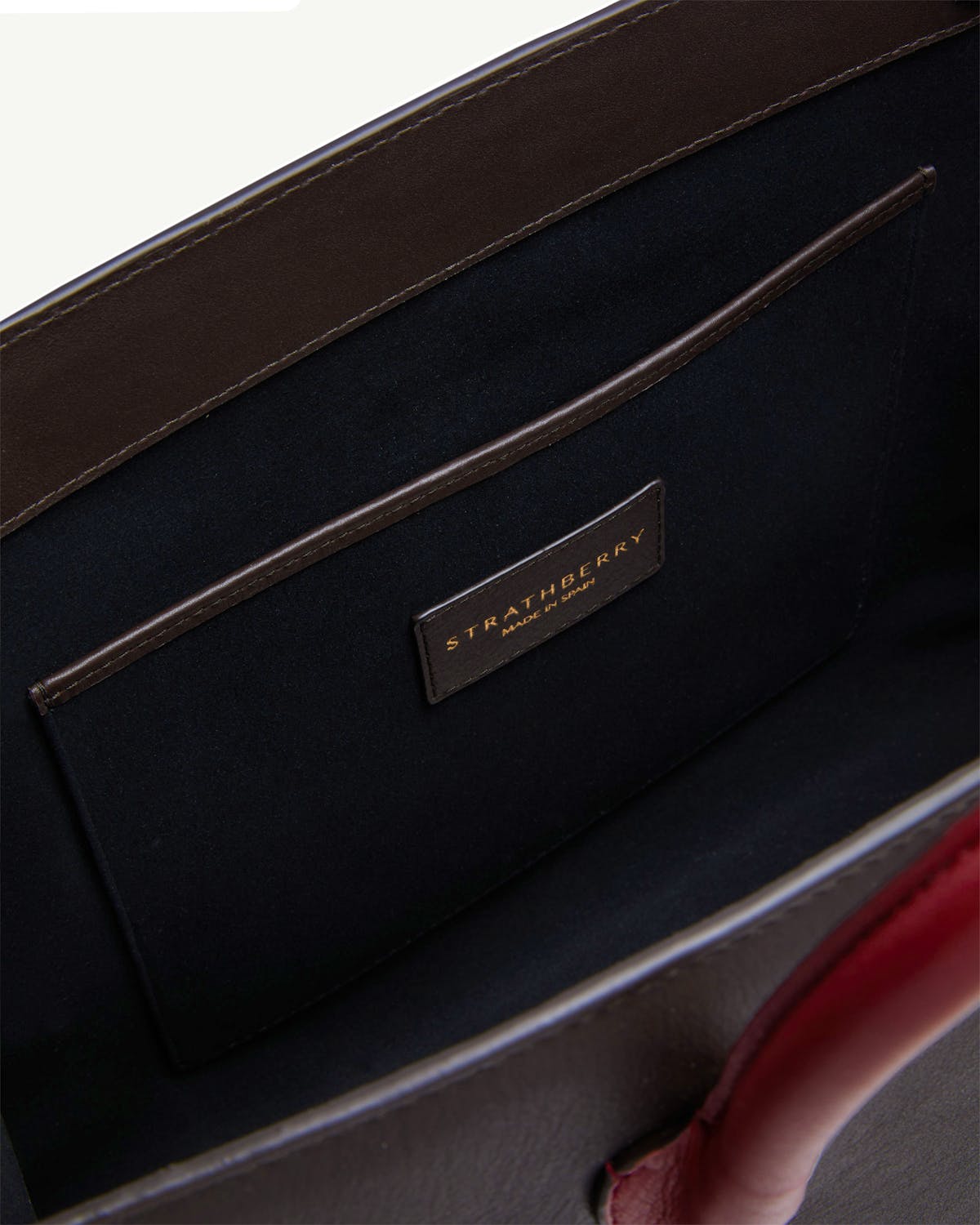 Tote interior with black lining, leather pocket, Strathberry gold logo, oxblood handle.