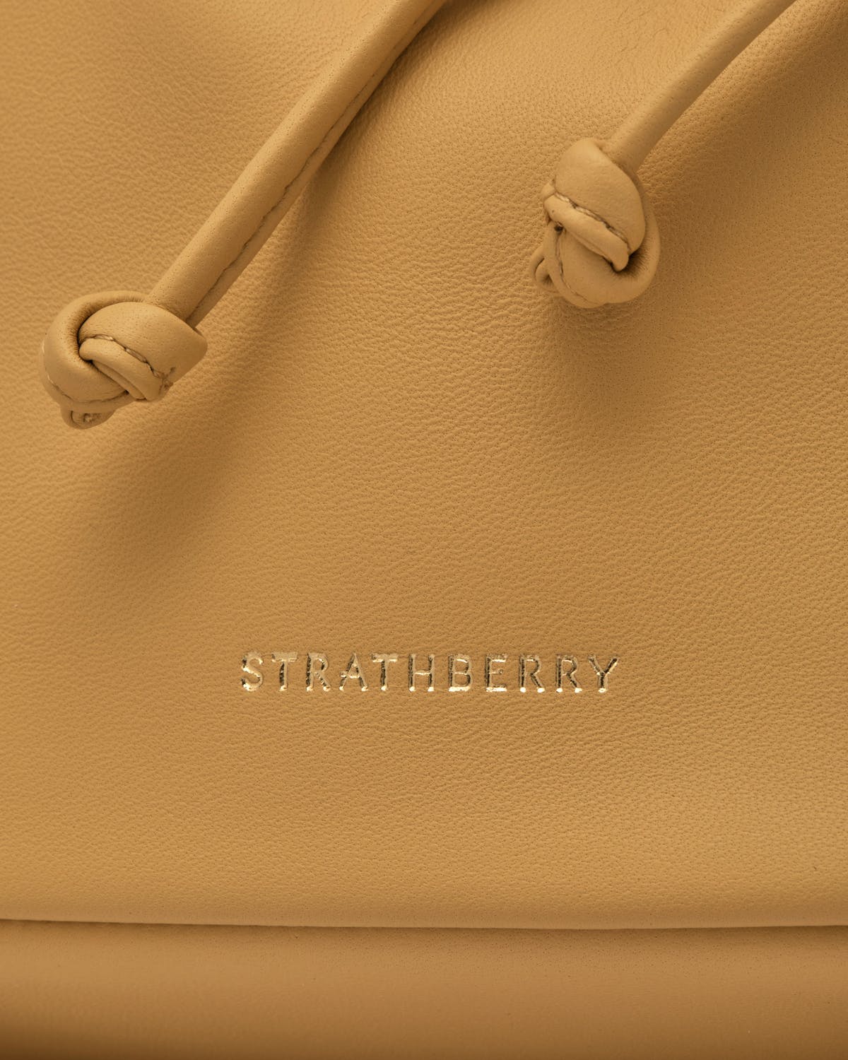 Brûlée leather Charlotte Drawstring bag showing knotted drawstrings and Strathberry logo.