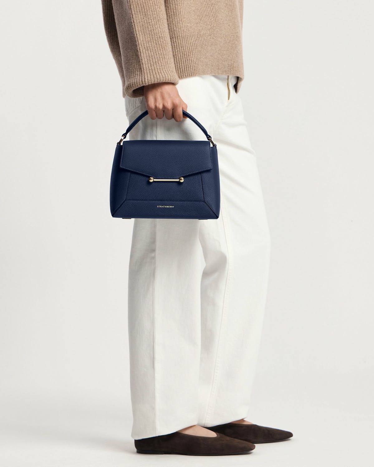 Model waist-down holding navy mosaic bag by Strathberry with gold bar detail.