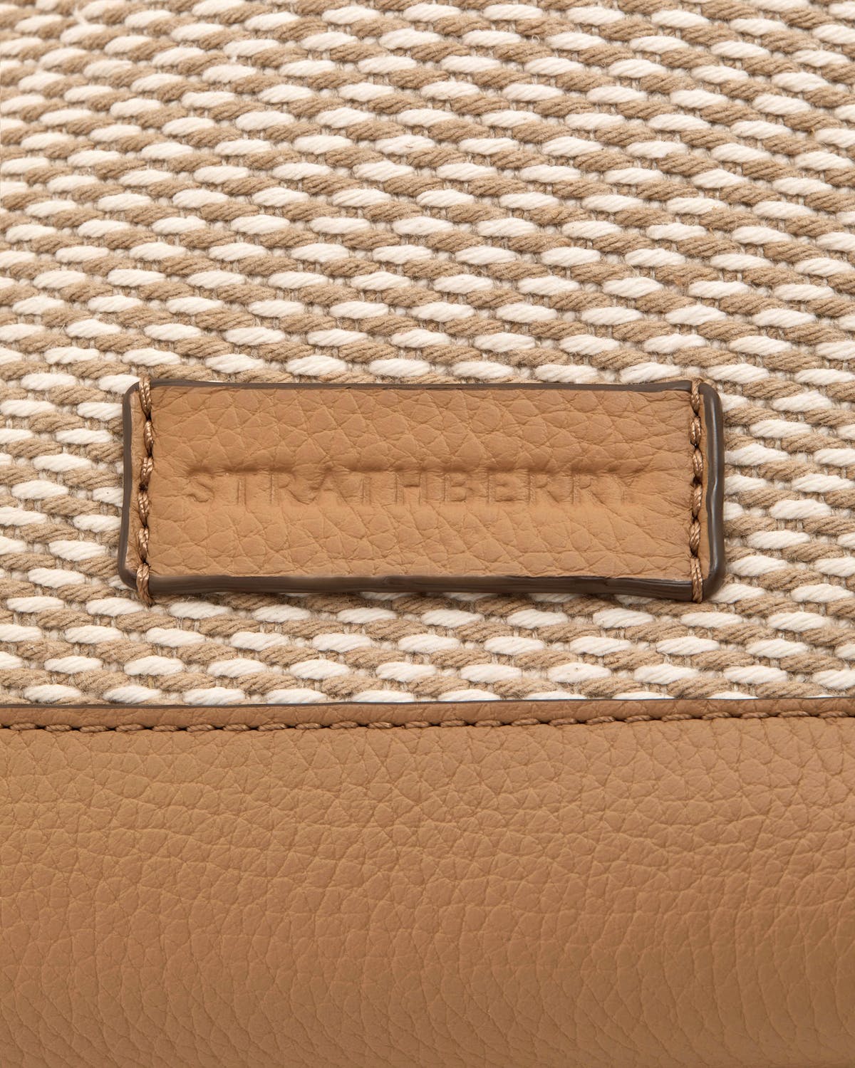 Caramel leather label embossed 'Strathberry' on natural twill fabric panel.