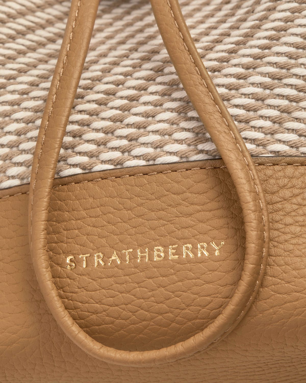 Strathberry logo on caramel pebbled leather with natural twill background.