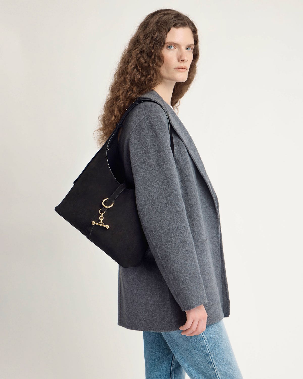 Woman wearing black suede Kite Hobo bag over shoulder with grey coat and jeans
