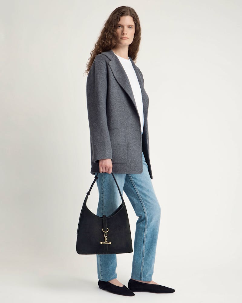 Model carrying black suede Kite Hobo bag with gold hardware, wearing grey coat.