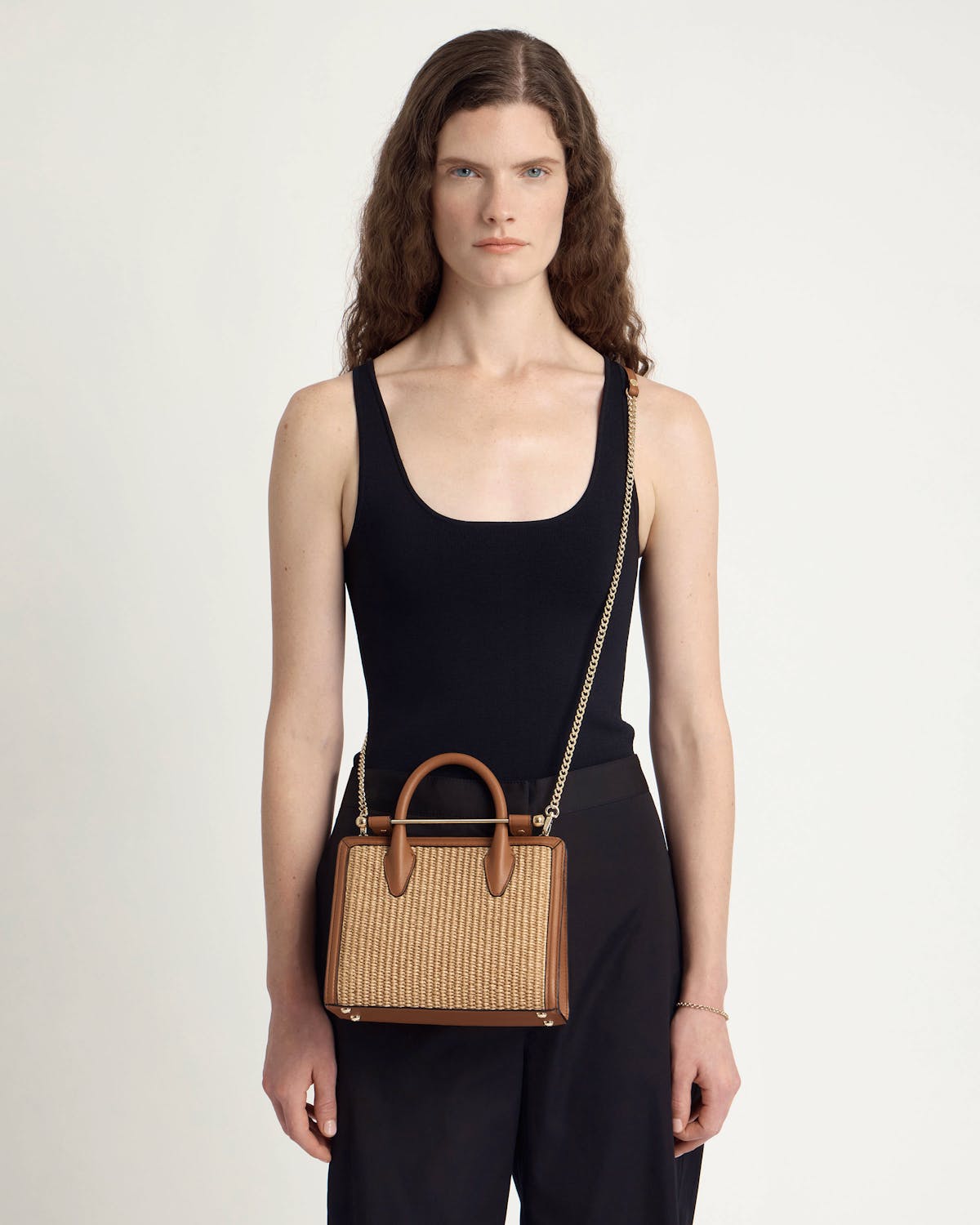 Model wearing tan and natural raffia mini tote with gold chain strap and handles.