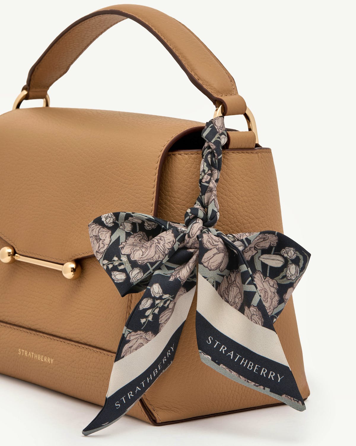 Black and oat floral silk skinny scarf tied to tan leather bag handle, Strathberry.