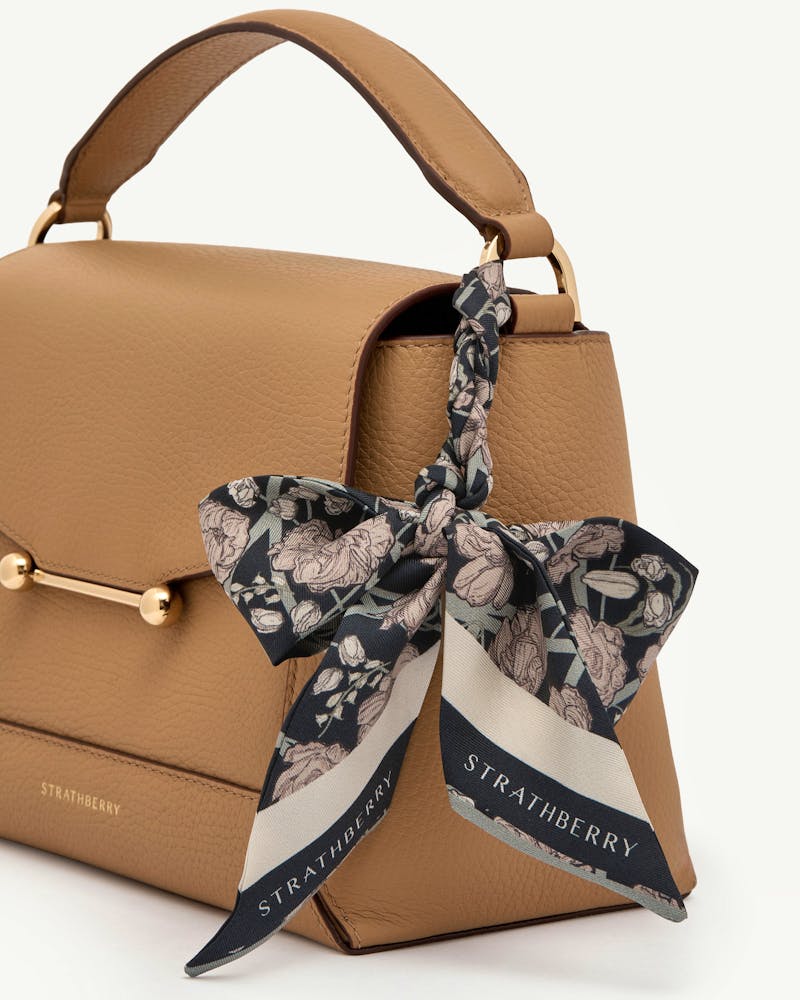 Black and oat floral silk skinny scarf tied to tan leather bag handle, Strathberry.